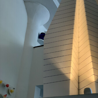 Detail of corner of the apartment with view of tall, white decorative piece with vertical black lines evenly distributed raising towards the ceiling.