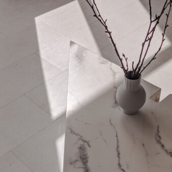 Modern design. Close-up of triangular coffee table in white and grey marble with white vase and ornamental branches.