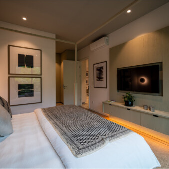 Modern bedroom design, with clean lines and simple shapes. White walls and queen bed with white bed cover adorned with pillows in grey and black with and without patterns. Walls have abstract images in black with white matting and simple black frames.