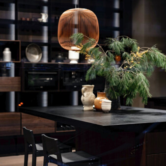 Dining room area with mostly black and dark wood table and chairs, with hanging lamp coming from a tall ceiling.