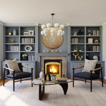Small living room with two chairs in black fabric, and black wood frame, with a striped decorative pillow. Large, wall-to-wall unit is painted in grey, and has a fireplace in the middle. Modern table with black base in the middle has decorative objects in black, white and gold to match other pieces around the room.